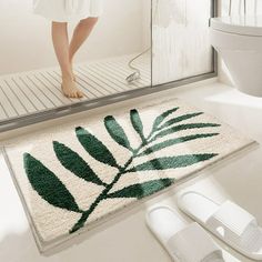 a bathroom rug with a green leaf on it and white slippers next to it