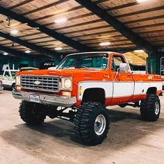 an orange and white truck parked in a garage with big tires on it's tires