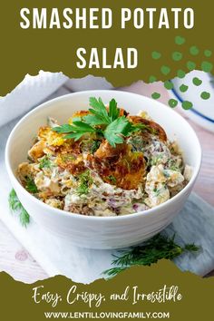 Smashed potato salad garnished with parsley and dill with plates and fork in the background.