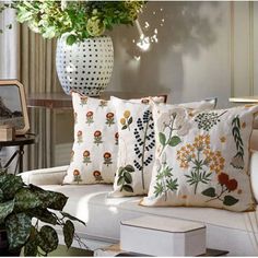 three pillows on a white couch next to a potted plant