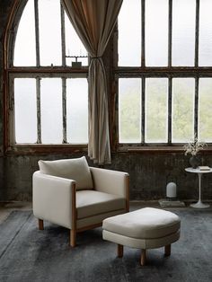 a chair and ottoman in front of large windows