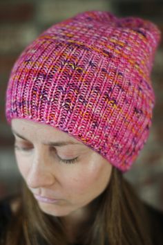 a woman wearing a pink and orange knitted hat looking down at her cell phone