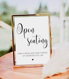 an open seating sign sitting on top of a wooden table next to a white feather