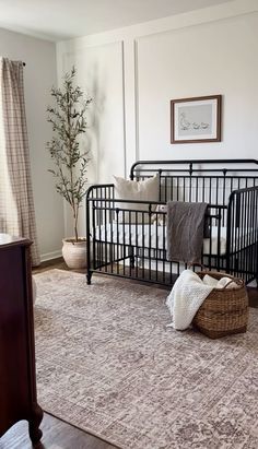 Neutral nursery inspo, black crib, loloi rug, olive tree, planter, wicker blanket basket, waffle blanket, throw blanket, throw pillow, checkered curtains, nursery rug, nursery curtains, nursery wall art Dark Floor Nursery Ideas, Creamy White Nursery, Nursery Couch Ideas, Nursery Rug Placement Layout, Nursery Ideas Renter Friendly, Neutral Cozy Nursery, Black Trim Nursery, Nursery Walls Ideas, Nursery Simple Neutral