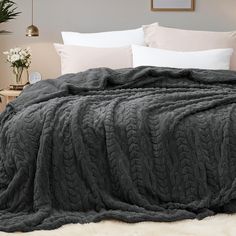 a bed covered in a gray blanket and pillows with white pillows on top of it