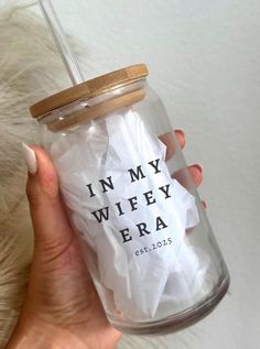 a person holding a clear glass with white tissue in it and the words in my wheyy era printed on it