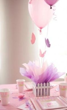 a pink table topped with plates and cups filled with cake next to a bunch of balloons