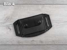 a black leather belt case on a white wooden background with the word black written across it