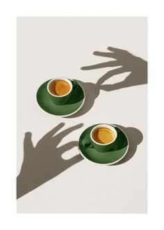 two cups of coffee are sitting next to each other on saucers with their shadows