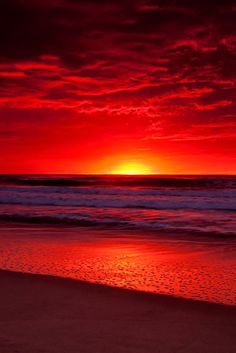 the sun is setting over the ocean with red clouds