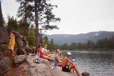 a group of people sitting on top of a rock next to a lake