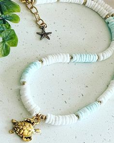 a turtle and starfish necklace on a white table next to a potted plant