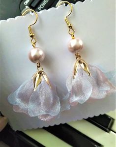 two pairs of earrings with pink flowers and pearls hanging from the earwires on a piano