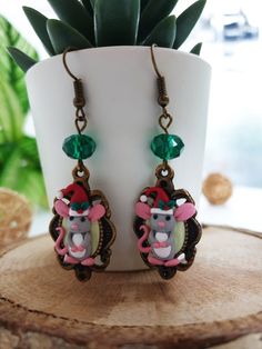 a pair of earrings with an image of a mouse on it sitting next to a potted plant