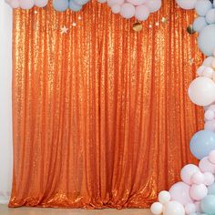 an orange backdrop with balloons and streamers on the floor in front of a curtain