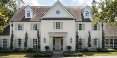 a large white house with lots of windows and plants on the front door, surrounded by greenery