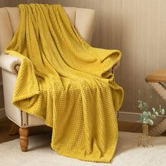 a chair with a yellow blanket on it next to a white rug and wooden table