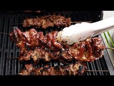 several skewers of meat are being cooked on a bbq grill with tongs