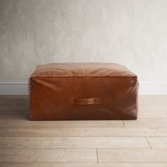 a brown leather ottoman sitting on top of a hard wood floor next to a white wall