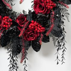 red and black flowers are arranged on a white wall with greenery, berries and leaves