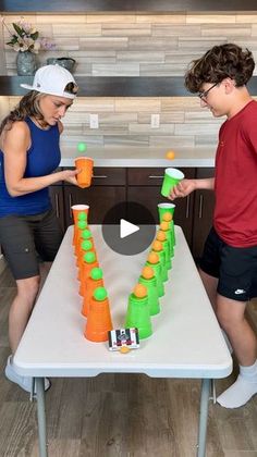 two people standing in front of a table with orange and green cups on it,