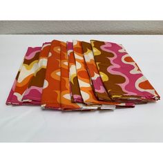 four pieces of cloth folded together on a white tablecloth covered with pink, orange and brown designs