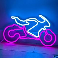 a neon sign with a motorcycle on it in the middle of a floor next to a blue wall