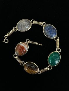 Antique Art Deco 14k Gold Multi-Gemstone Carved Scarab Bracelet 7.5"  Item here is an antique Art Deco 14k gold multi-gemstone carved scarab bracelet. This bracelet features stones such as sardonyx, tiger's eye, chalcedony, lapis, and quartz. Bracelet is marked 14k gold and closes with a spring ring.  Condition: Good; item is pre-owned and may have some signs of light use and age related wear. Please look closely at the pictures provided as they are an extension of our written description. Measurements: Length: 7.5 in Width: .5 in Weight: 8.4 dwt 8731F Antique Multi-stone Bracelet For Formal Occasions, Antique Multi-stone Bracelets For Formal Occasions, Antique Multi-stone Bracelet As Gift, Antique Multi-stone Bracelets As Gift, Heirloom Multi-stone Bracelets For Formal Occasions, Vintage Oval Multi-stone Bracelets, Vintage Gold Cabochon Gemstones, Classic Oval Multi-stone Bracelet, Antique Round Gemstone Bracelets