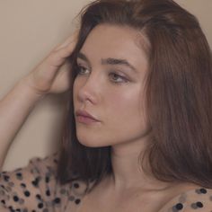 a woman with brown hair and polka dot shirt holding her hand to her head while looking off into the distance