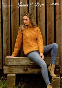 a woman sitting on top of a wooden bench wearing a yellow sweater and blue jeans