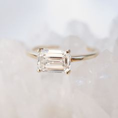 an emerald cut diamond ring sitting on top of a rock