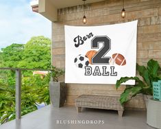 a banner that says born 2 ball hanging from the side of a building with plants in front of it