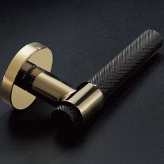 a close up of a metal object on a black surface with a gold colored handle