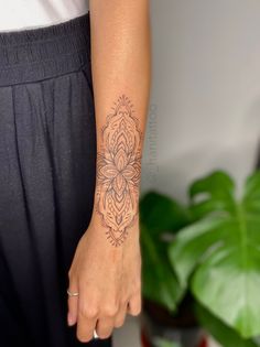 a woman's arm with a tattoo on her left hand and a plant in the background