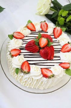 a white cake with strawberries and cream frosting on a plate next to flowers