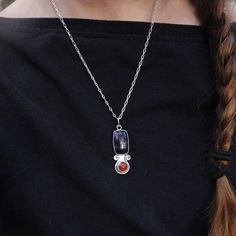 a woman wearing a black shirt has a silver necklace with two red stones on it