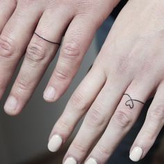 two fingers with small tattoos on them, one has a heart and the other has an arrow