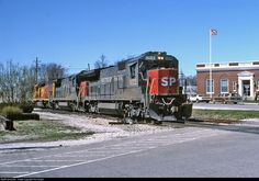 a train traveling down tracks next to a building and flag pole in front of it