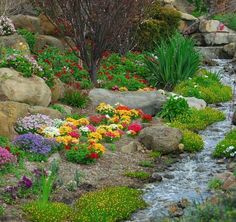 a garden filled with lots of flowers next to rocks and water flowing down it's side