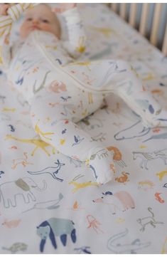 a baby laying in a crib with an elephant print sheet on it's side