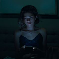 a woman sitting in the dark looking at her cell phone