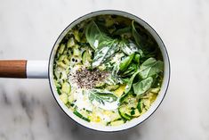 a pot filled with green vegetables on top of a white counter next to a wooden spoon