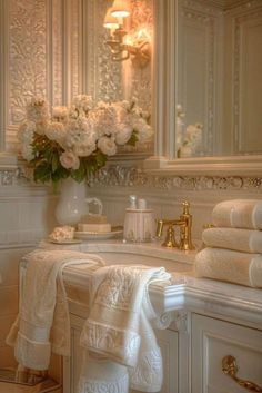 a bathroom with white towels stacked on top of the sink next to a vase filled with flowers