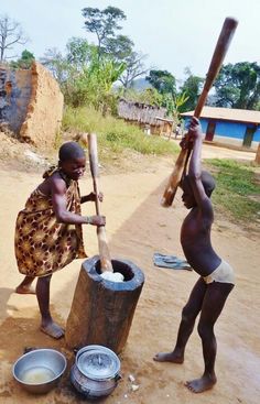 two children are playing with buckets and baseball bats on the dirt road in front of their home