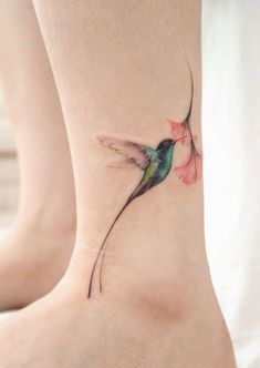 a small hummingbird tattoo on the ankle with pink flowers in it's beak