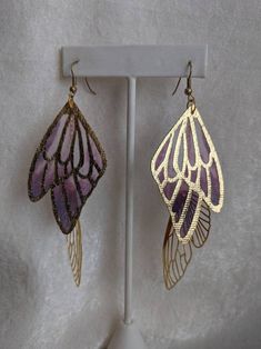 These unique and whimsical earrings feature gorgeous colored and golden faerie wings. Perfect for special occasions or to add a bit of magic to your everyday! Choose primary color between lavender/purple, aqua/sapphire, teal/purple, or purple/red! Whimsical Purple Nickel-free Earrings, Whimsical Nickel-free Purple Earrings, Whimsical Purple Drop Earrings, Fairycore Gold Drop Earrings, Purple Fairycore Jewelry For Party, Gold Fantasy Earrings For Party, Whimsical Handmade Purple Earrings, Whimsical Iridescent Earrings With Ear Wire, Gold Fairy Style Handmade Earrings