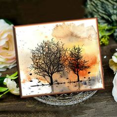 a card with watercolor trees on it and flowers in the background, sitting on a table