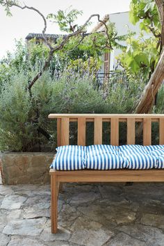 a wooden bench sitting on top of a stone floor next to a tree and bushes