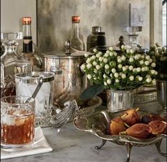 a table topped with lots of silver dishes filled with food and drinks next to vases full of flowers