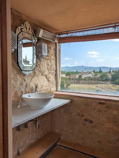 a bathroom with stone walls and a large window looking out at the countryside outside it